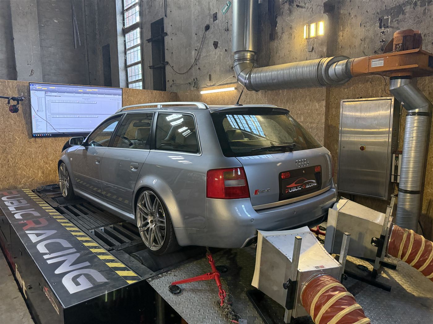 Silberner Audi Avant auf dem Allradprüfstand mit angeschlossener Abgasabsaugung.