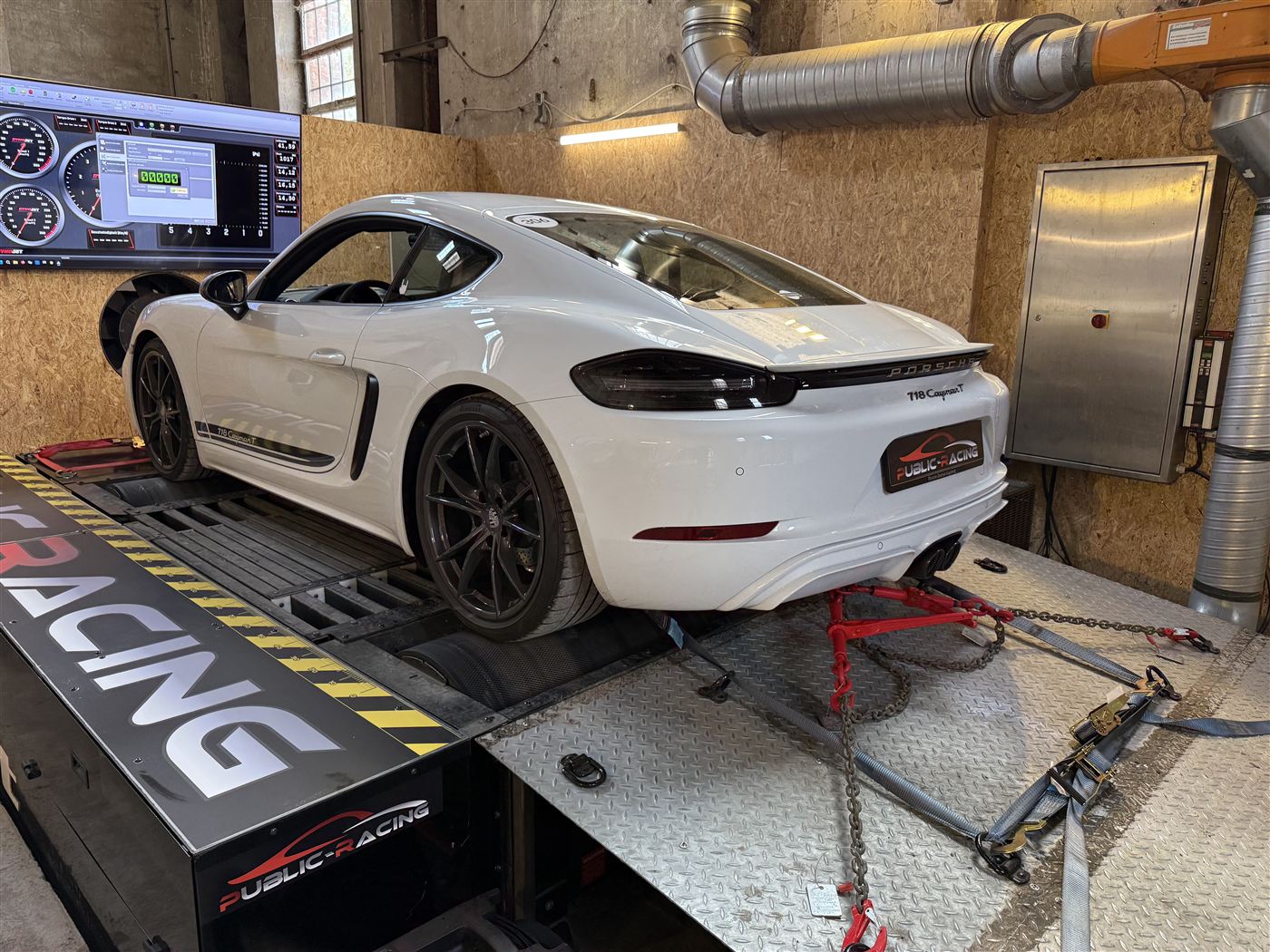 Weißer Porsche 718 Cayman GTS auf dem Allradprüfstand, angezurrt, mit Messbildschirm im Hintergrund.