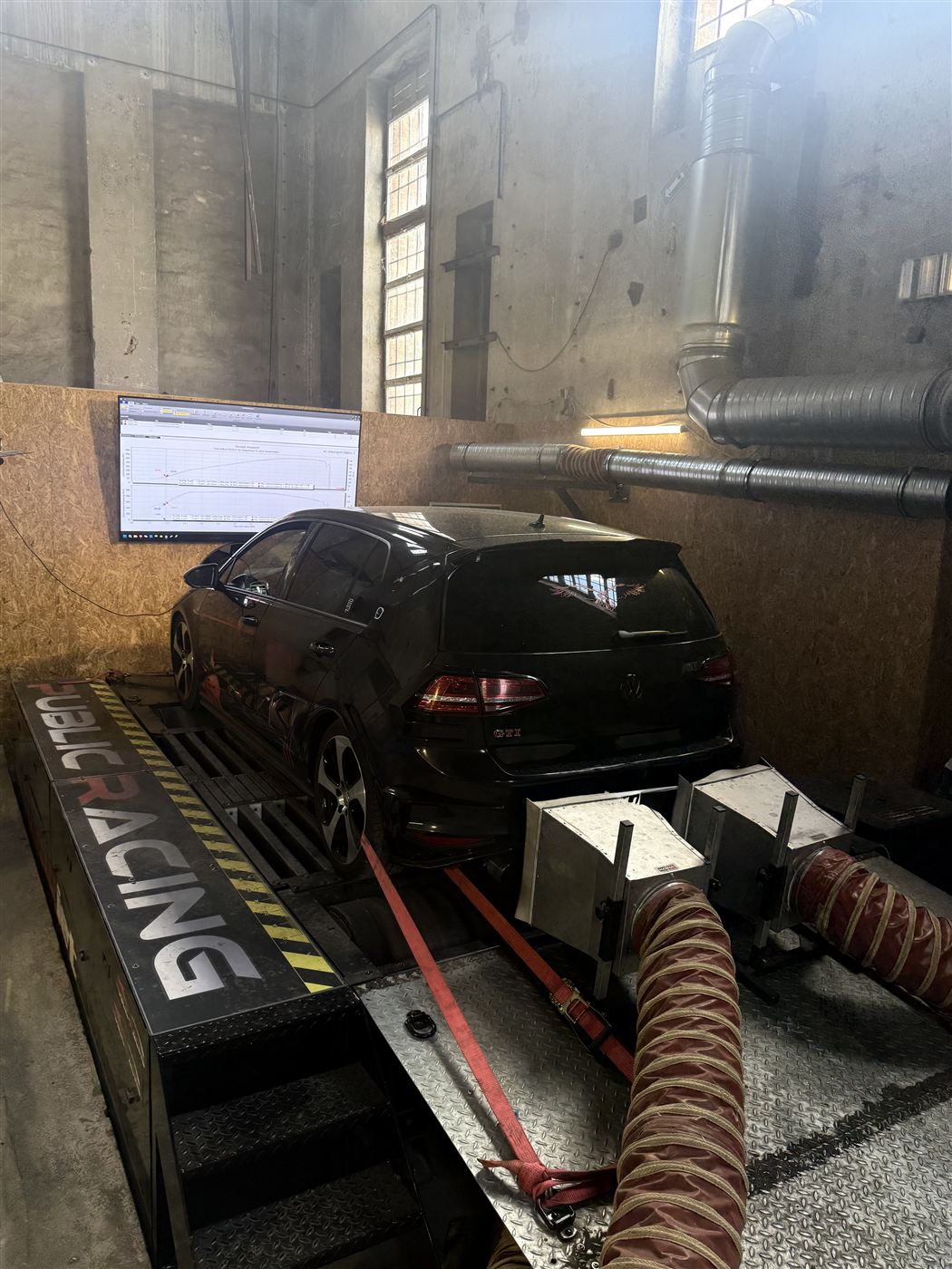 Schwarzer VW Golf GTI auf dem Prüfstand, darüber der Bildschirm mit dem Messdiagramm.
