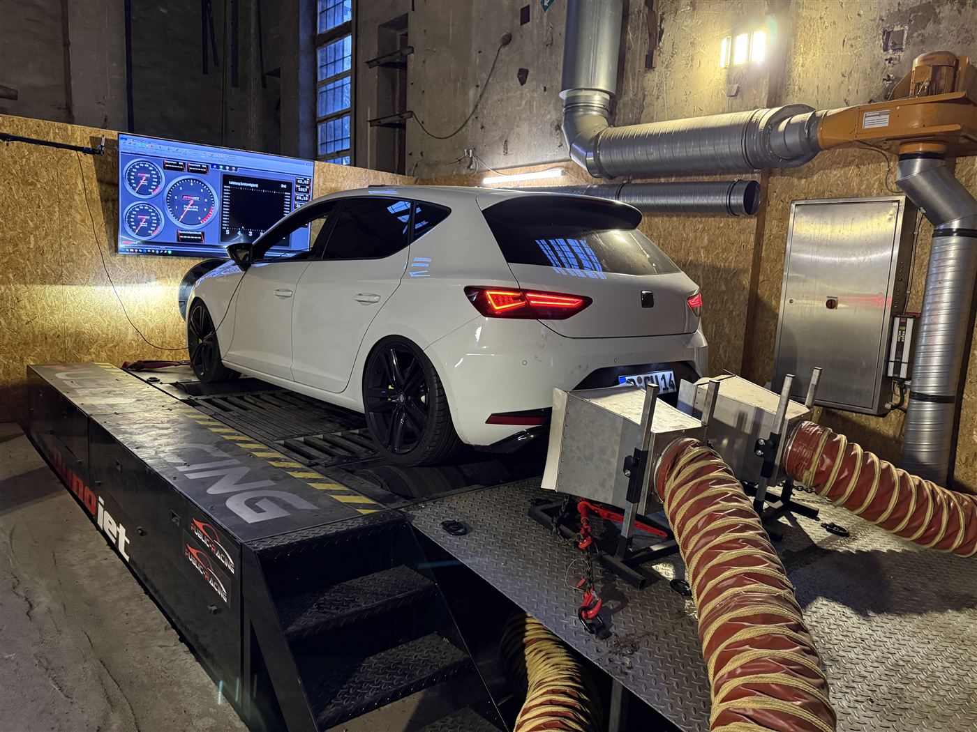 Weißer Seat Leon auf dem Leistungsprüfstand, daneben zwei Bildschirme mit den Messwerten.