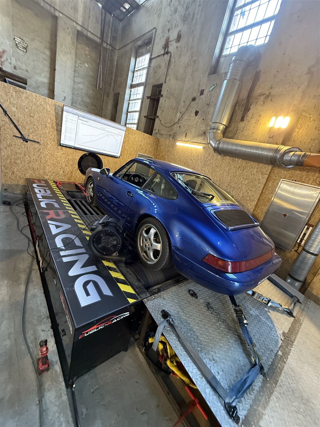 Blauer Porsche 964 auf dem Prüfstand, im Hintergrund der Bildschirm mit der Leistungskurve.